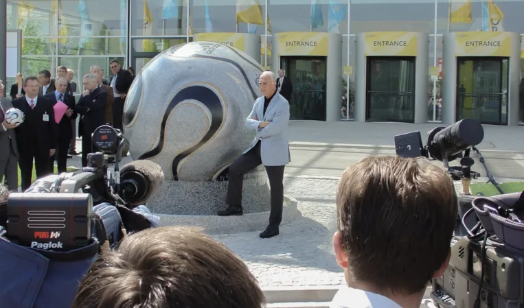 Franz Beckenbauer posing in front of a floating sphere designed like the official 2006 World Cup football