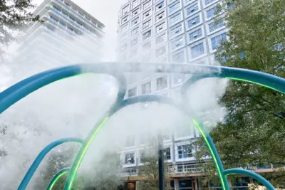 Curved blue and green fountain arches spraying water mist in an urban plaza