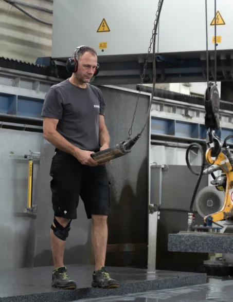 Worker handling a granite slab in a stone processing workshop