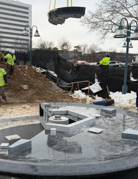 Granite fountain components being installed at a construction site with a crane lifting a circular stone element
