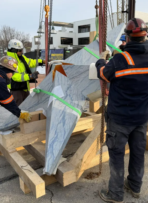 Construction workers positioning a prefabricated granite element with lifting straps at a construction site