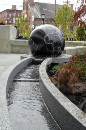 Polished black granite sphere fountain with a curved water channel in a landscaped urban setting