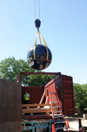 Polished black granite sphere being lifted by a crane during fountain installation