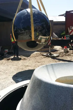 Polished black granite sphere being lifted into position above its fountain base during installation