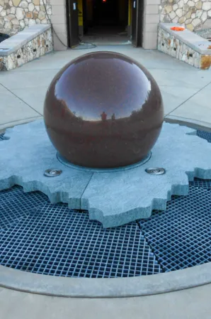 Polished granite sphere fountain on a circular stone base with surrounding water grille