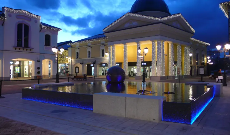 Illuminated granite fountain with a floating stone sphere in a reflecting pool at night