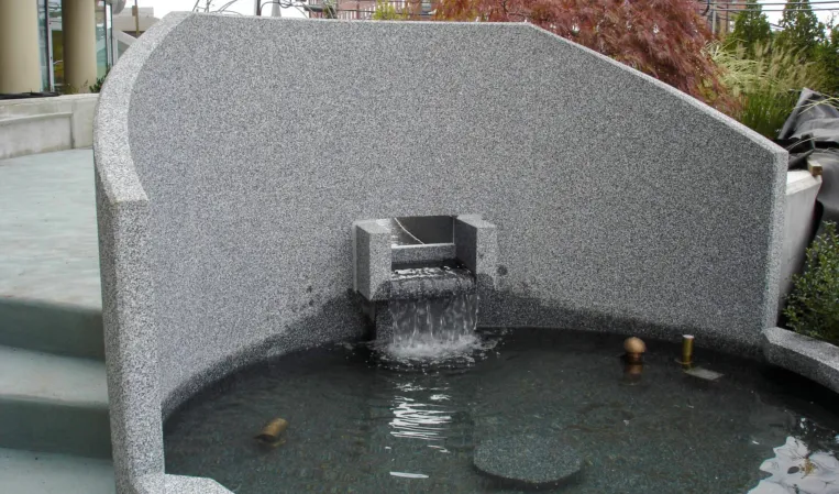 Granite fountain with a curved stone wall and integrated water spout cascading into a basin