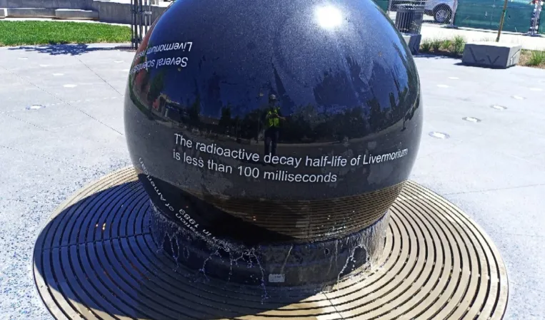 Polished black granite sphere fountain with engraved scientific text about radioactive decay