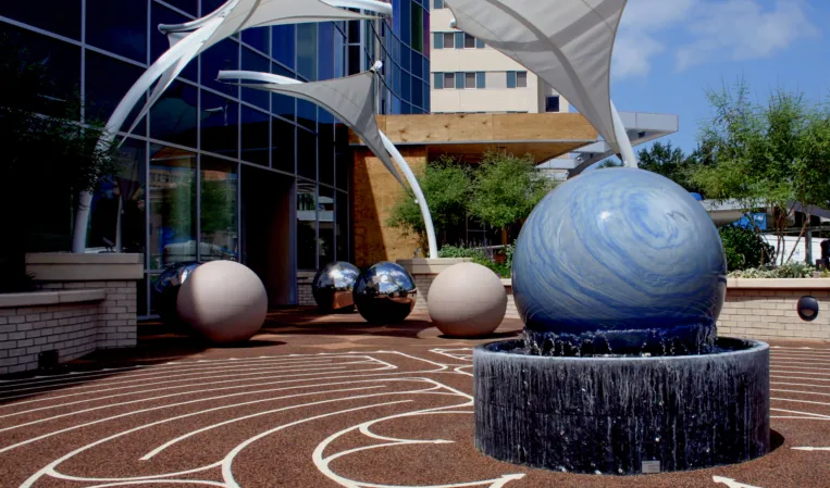 Blue granite sphere fountain in a modern urban plaza with sculptural shade sails