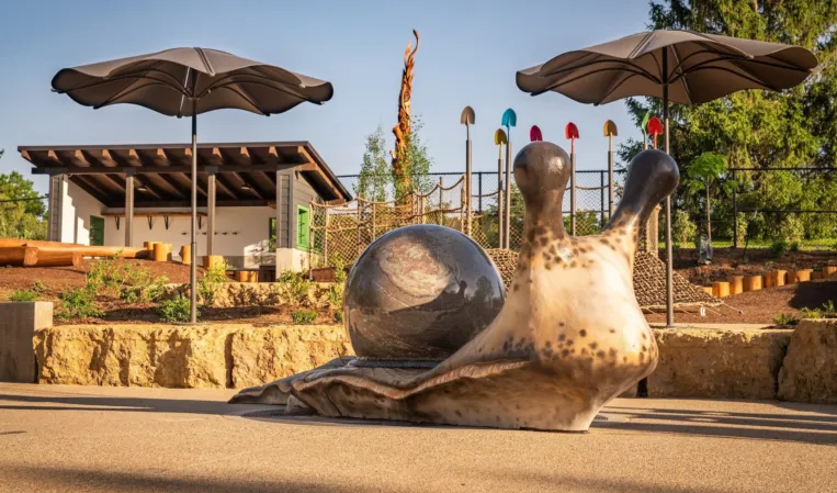 Granite sphere fountain beside a large sculptural snail in an outdoor playground