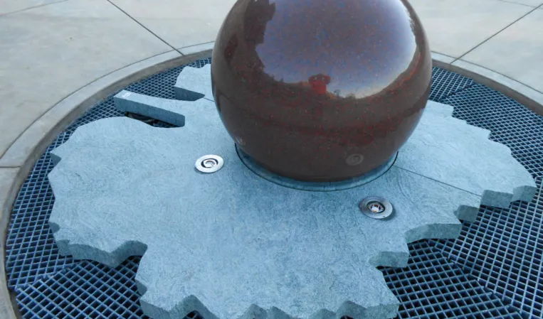 Polished granite sphere fountain on a circular stone base with surrounding water grille