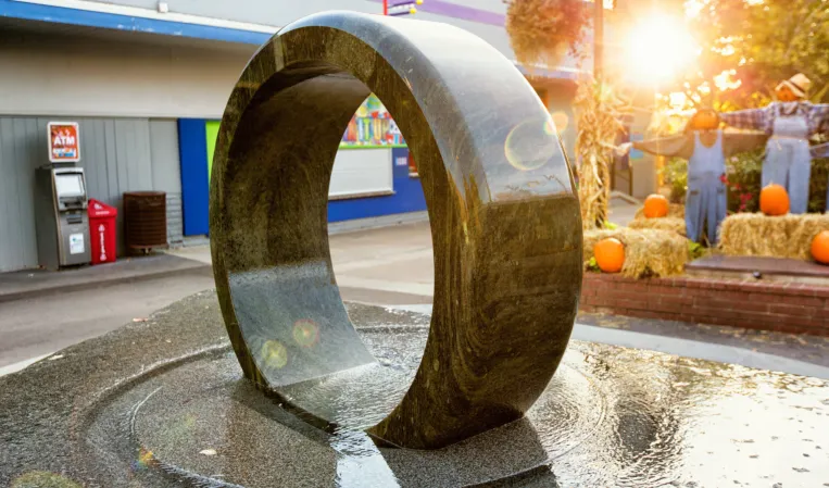 Polished granite ring fountain in an outdoor plaza with autumn trees in the background