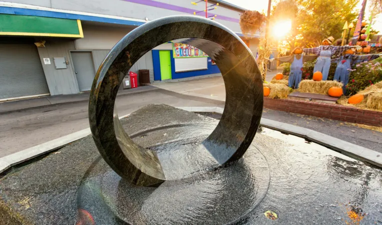 Polished granite ring fountain in an outdoor plaza with autumn trees in the background