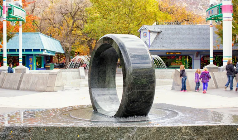 Polished granite ring fountain in an outdoor plaza with autumn trees in the background