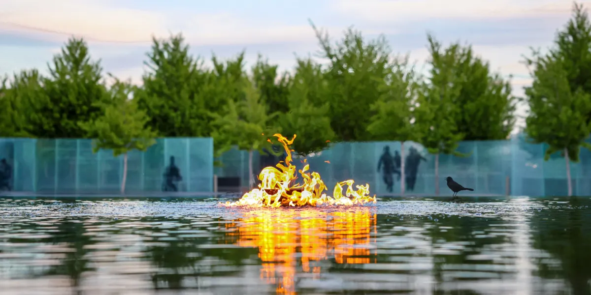 fire in the center of a reflecting pool surrounded by trees and glass panels