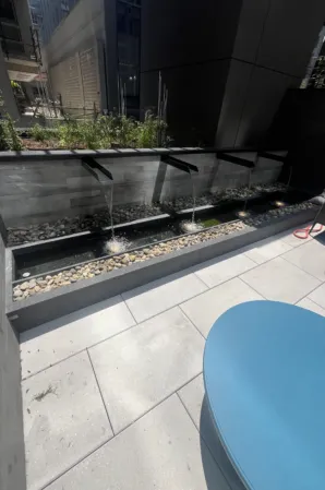 Granite water wall with angled spouts and pebble-filled basin in a modern courtyard