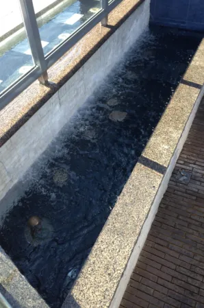 Narrow granite water channel with dark flowing water beside a glass railing