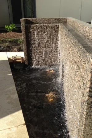 Granite water wall with cascading water flowing into a dark basin