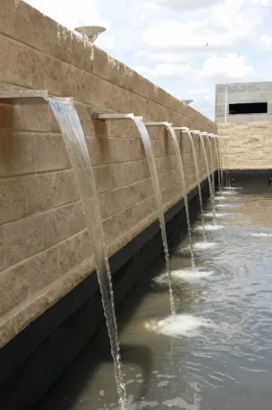 Water flowing from evenly spaced spouts in a natural stone wall into a long, rectangular reflecting pool.