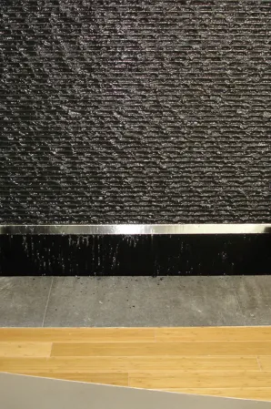 Close-up of textured black granite water wall with cascading water flowing into a basin
