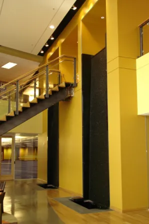 Tall black granite water wall beneath a staircase in a modern building interior
