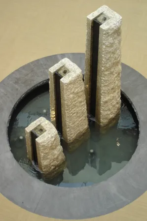 Top view of three rough-hewn granite pillars with water outlets in a circular indoor fountain basin