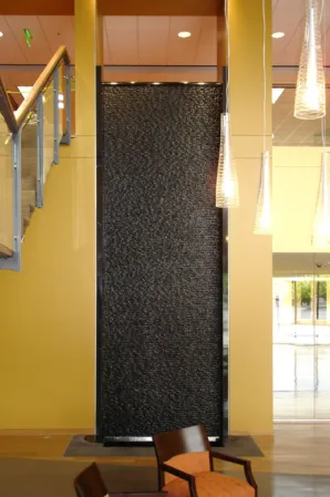 Tall black granite water wall with cascading water in a modern interior beside a staircase