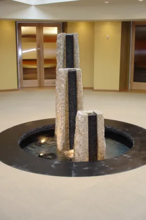 three rough-hewn granite pillars with water outlets in a circular indoor fountain basin