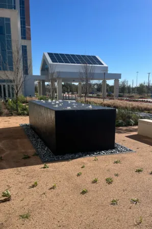 Black granite fountain with bubbling water jets in a landscaped outdoor area beside a modern building