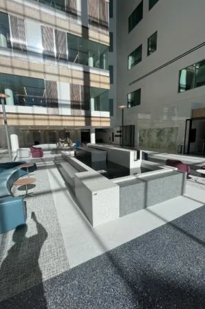 Geometric granite fountain with water basins and seating areas in a modern glass-walled atrium