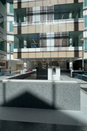 Geometric granite fountain with water basins and seating areas in a modern glass-walled atrium