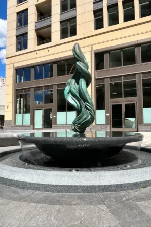 Bronze flame sculpture rising from a circular granite fountain in front of a modern office building