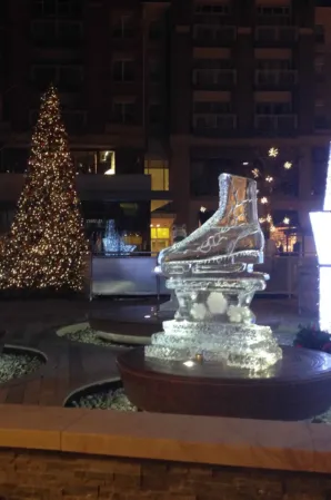 Illuminated ice skate sculpture fountain in a plaza decorated for Christmas at night