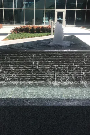 Granite fountain with a central water jet cascading over a textured stone wall into a lower basin