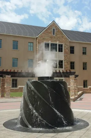 Black granite fountain with a spiral design and central water jet in front of a brick building