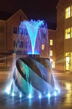 Illuminated black granite fountain with spiral design and blue water jets at night
