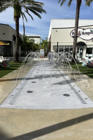 Arched water jets over a rectangular splash fountain in a palm-lined outdoor plaza
