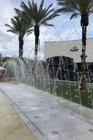 Arched water jets and illuminated splash fountains in a palm-lined outdoor plaza