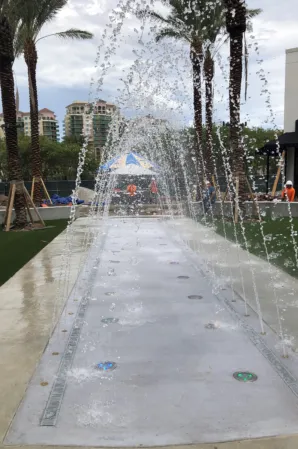 Arched water jets and illuminated splash fountains in a palm-lined outdoor plaza