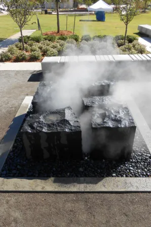 Three rough-hewn granite blocks with rising water mist in a rectangular fountain basin