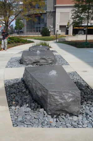 Sculptural granite blocks surrounded by decorative gravel in a landscaped urban plaza