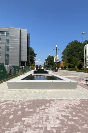 Long rectangular reflecting pool with granite edges along a paved walkway on a university campus