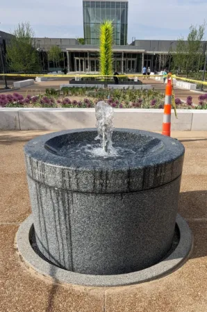 Circular granite fountain with a central water jet in a landscaped urban plaza