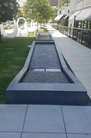 Long, narrow granite fountain basin with a sloped design beside a landscaped lawn