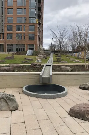 Narrow granite water channel flowing into a circular basin in a landscaped courtyard