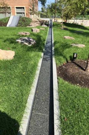 Narrow granite water channel running through a landscaped green space