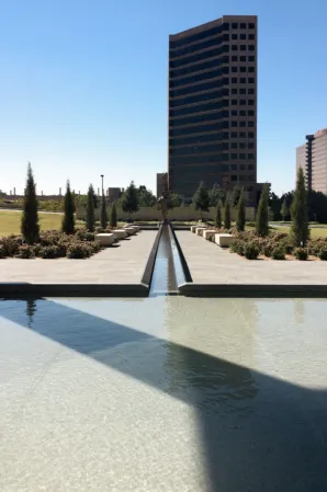 Long granite water channel connecting a reflecting pool to a landscaped plaza with modern office buildings in the background