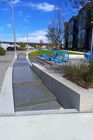 Long granite water channel with cascading sections beside a landscaped outdoor seating area