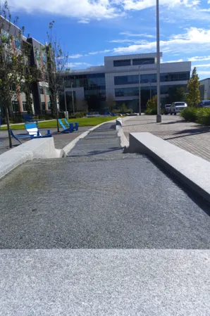 Long granite water channel with cascading sections beside a landscaped outdoor seating area