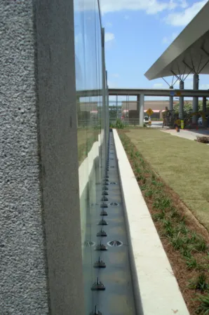 Narrow water channel with fountain nozzles alongside a glass wall in a landscaped courtyard
